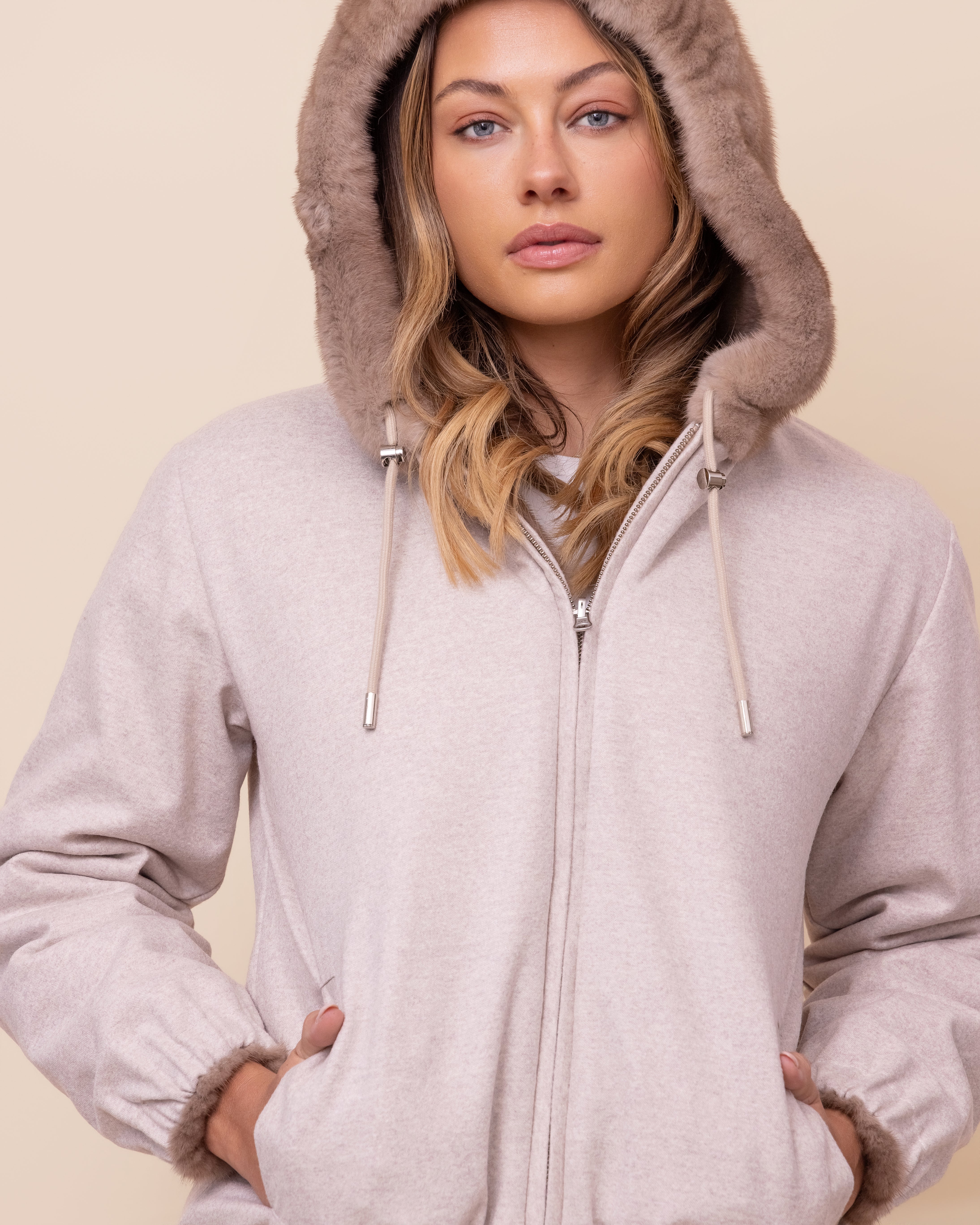 Woman wearing a beige hooded jacket against a plain background