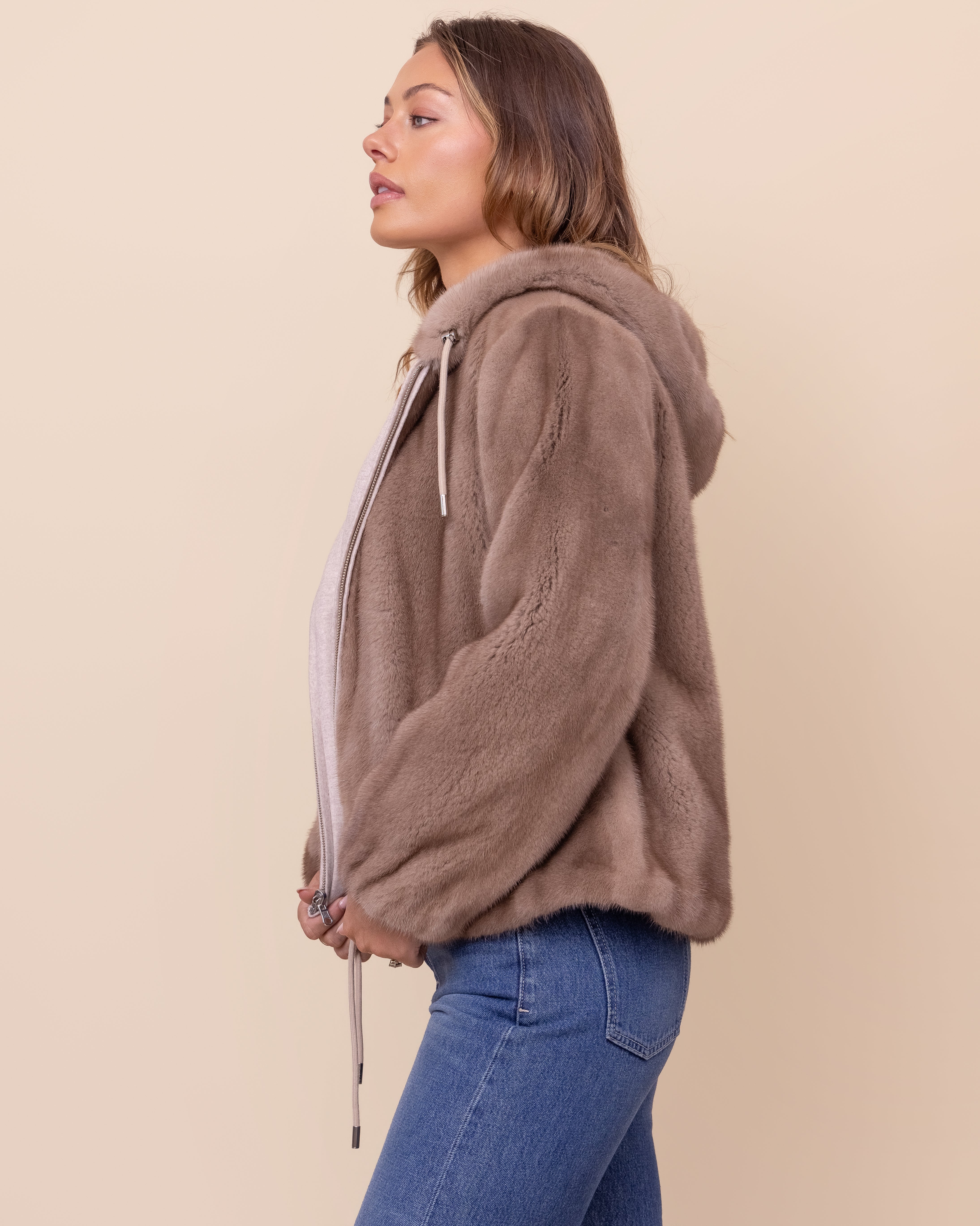 Woman wearing a brown mink jacket and blue jeans on a beige background