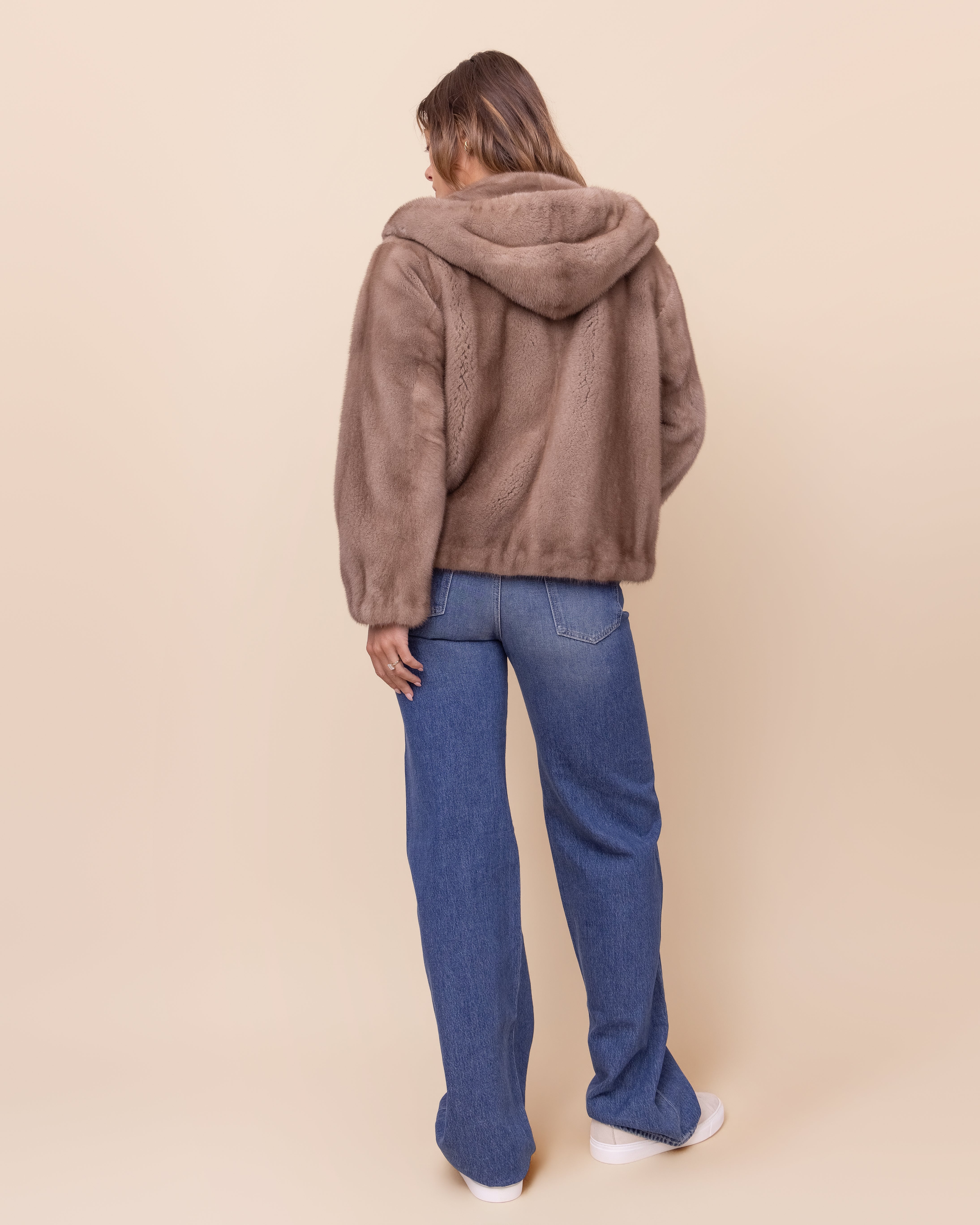 Person wearing a brown real fur jacket and blue jeans on a beige background