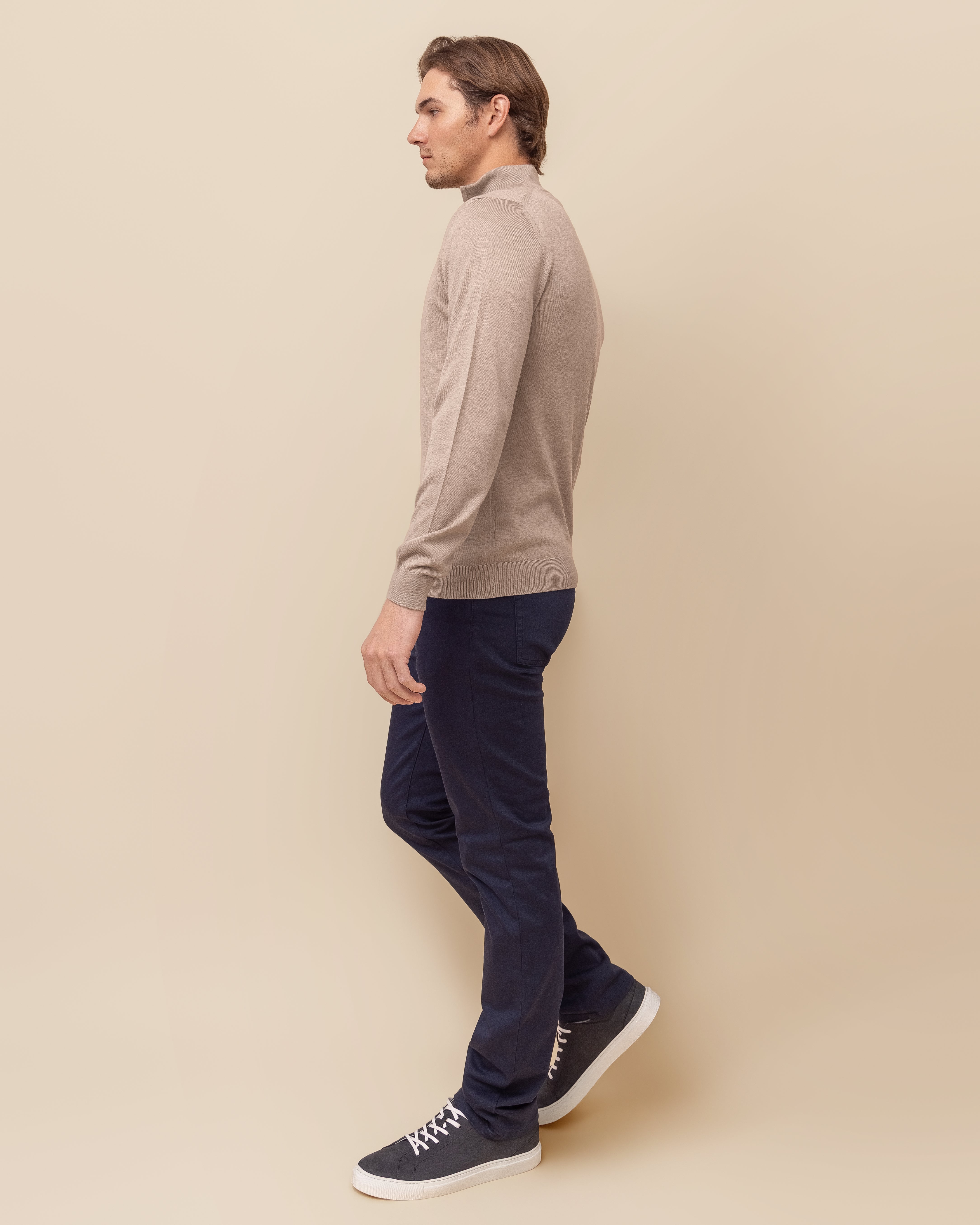 Man wearing a beige sweater and dark pants against a beige background