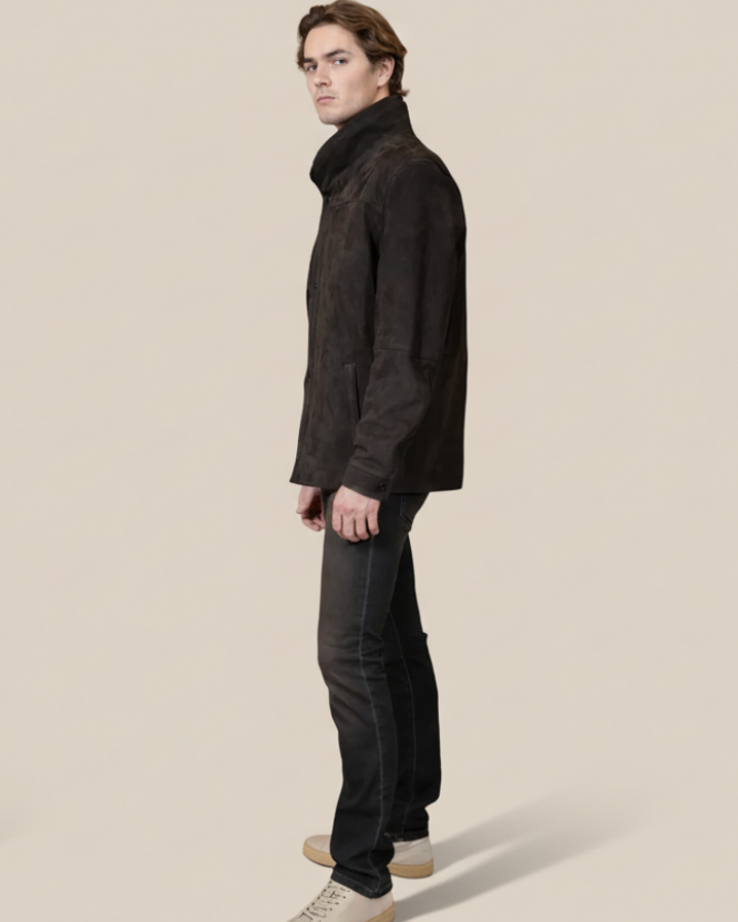 Man wearing a black coat and pants standing against a beige background