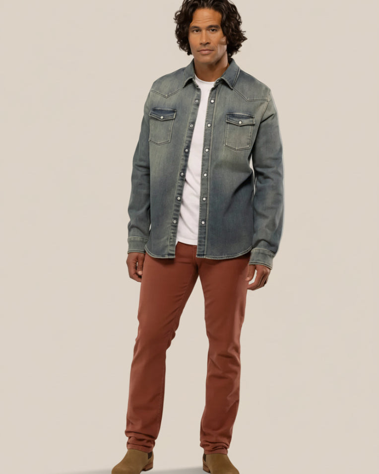 A man wearing a blue denim jacket and brown pants, standing against a plain background.