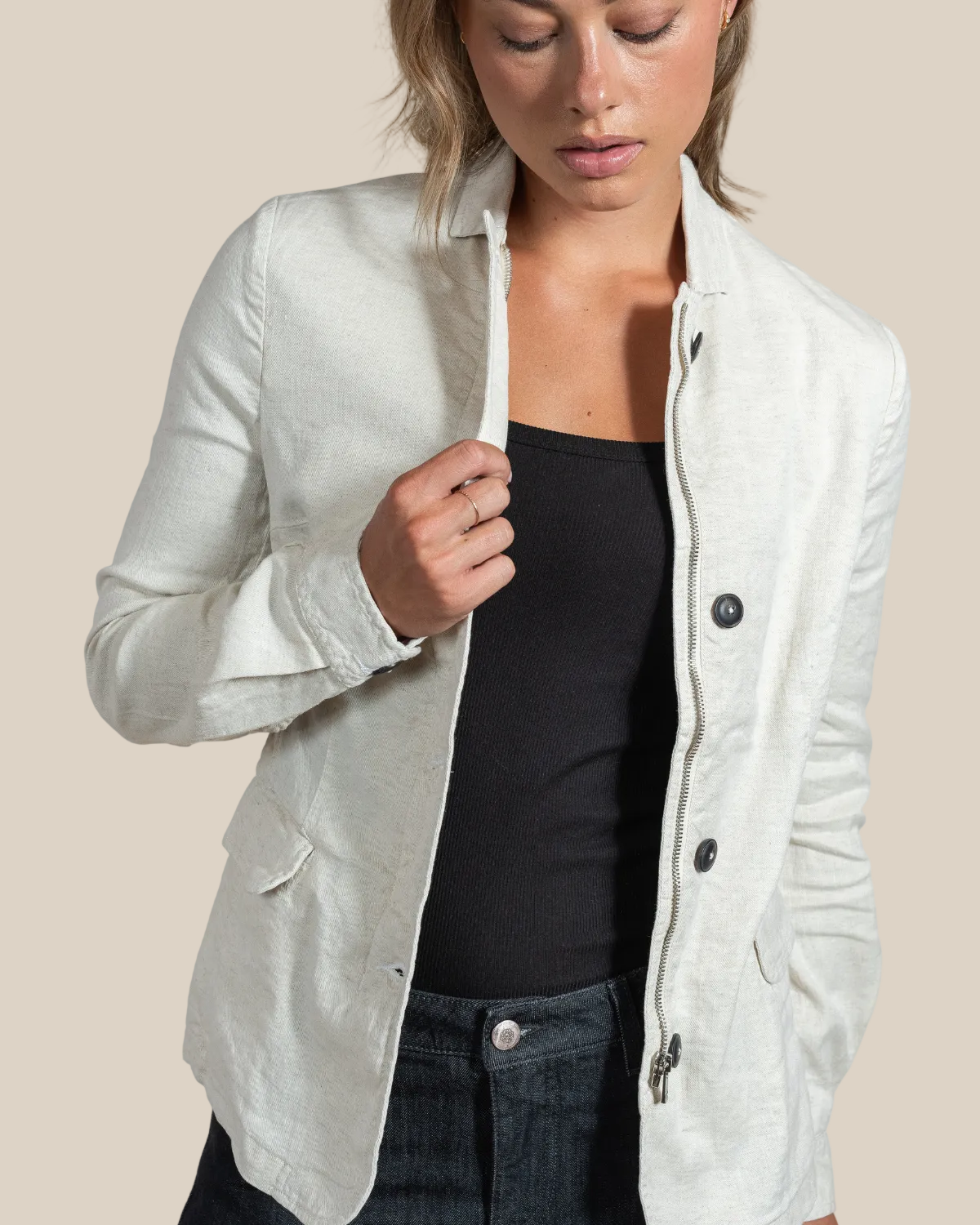Woman wearing a light gray jacket over a black top on a beige background