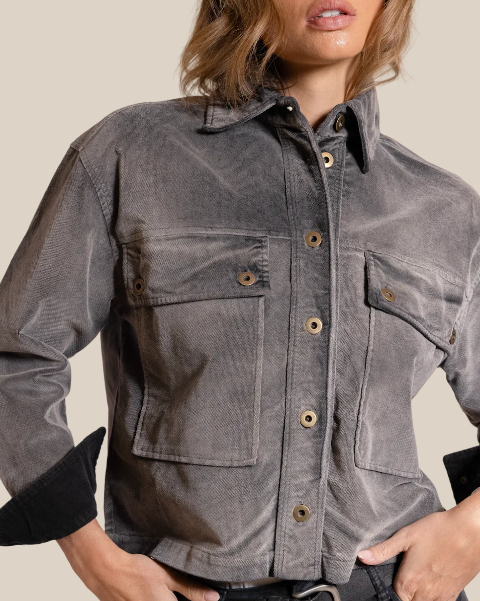 Person wearing a gray button-up shirt with black cuffs on a beige background