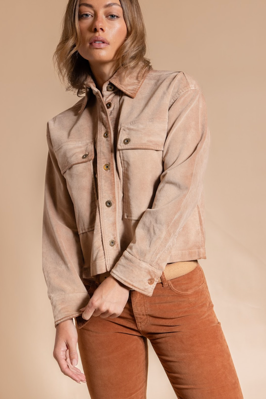 Woman wearing a beige jacket and brown pants against a beige background