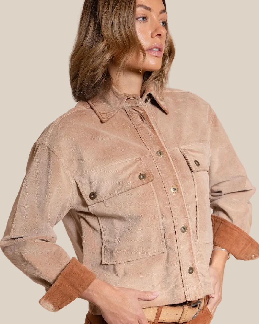 Woman wearing a beige jacket and brown pants against a beige background
