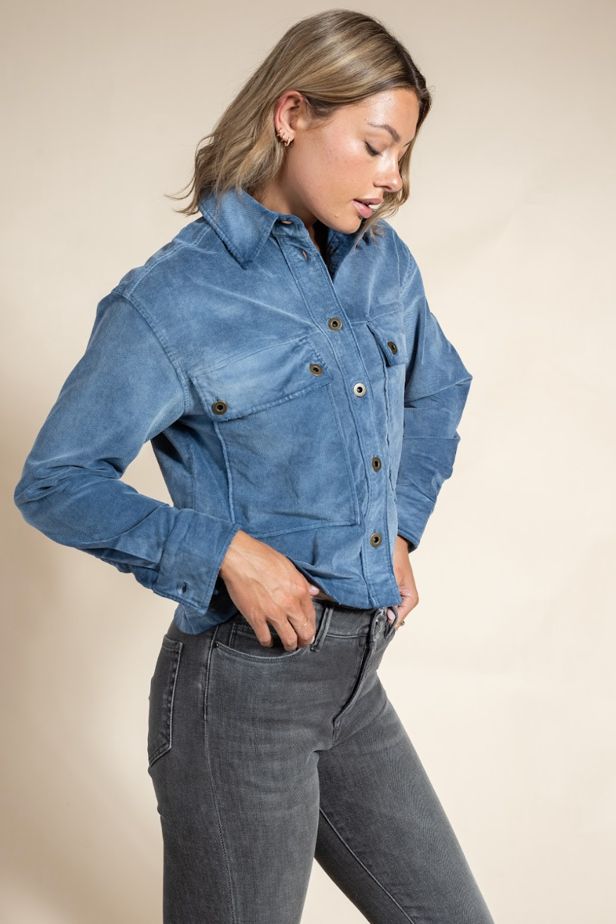 Woman wearing a blue denim jacket and gray jeans against a beige background