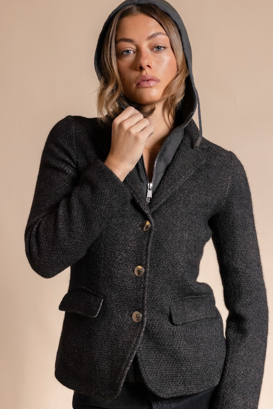 Woman wearing a dark gray hooded jacket against a beige background