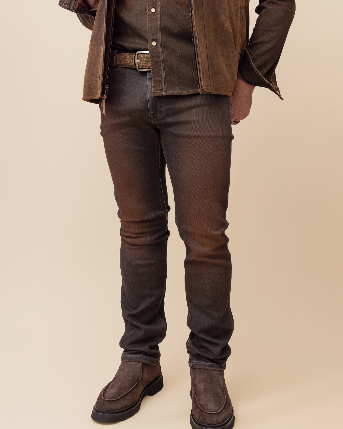 Person wearing a brown jacket, shirt, and jeans on a beige background