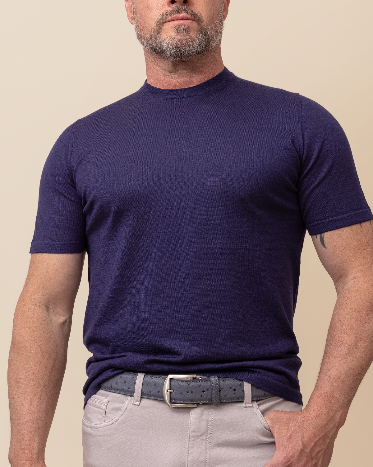Man wearing a navy blue t-shirt and light gray pants against a beige background