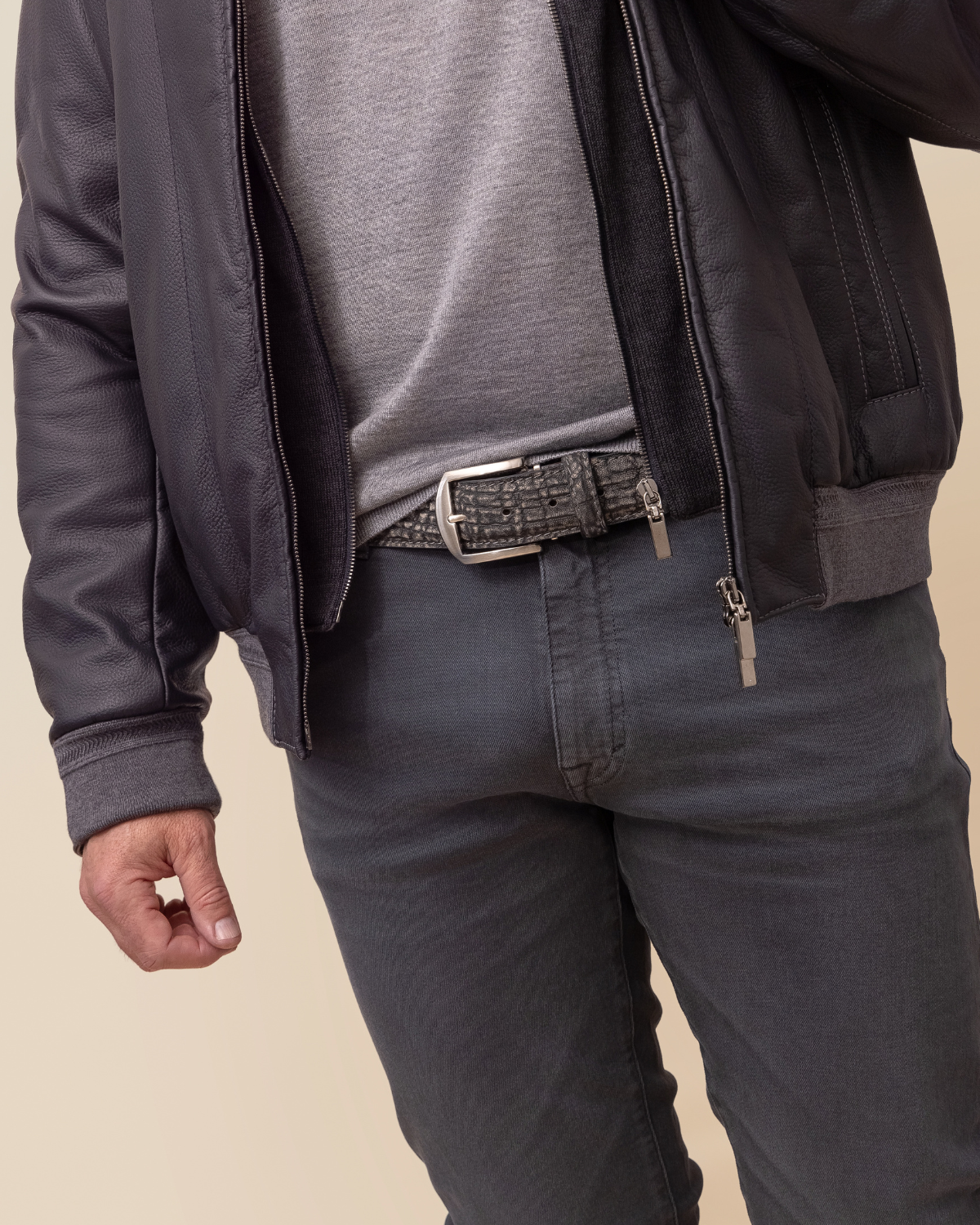 Person wearing a dark jacket, gray shirt, and dark pants on a beige background