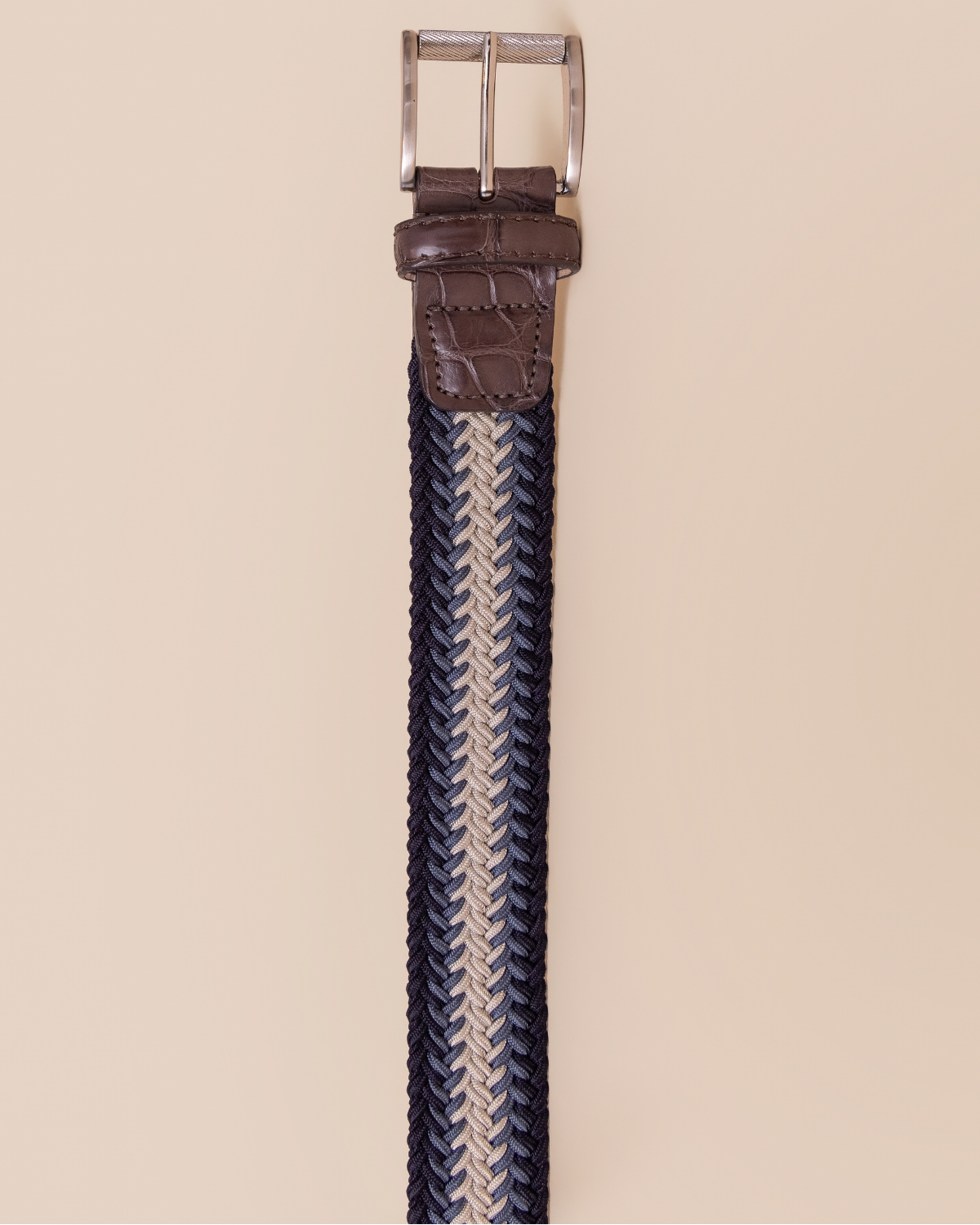 Braided belt with brown leather end and silver buckle on a beige background