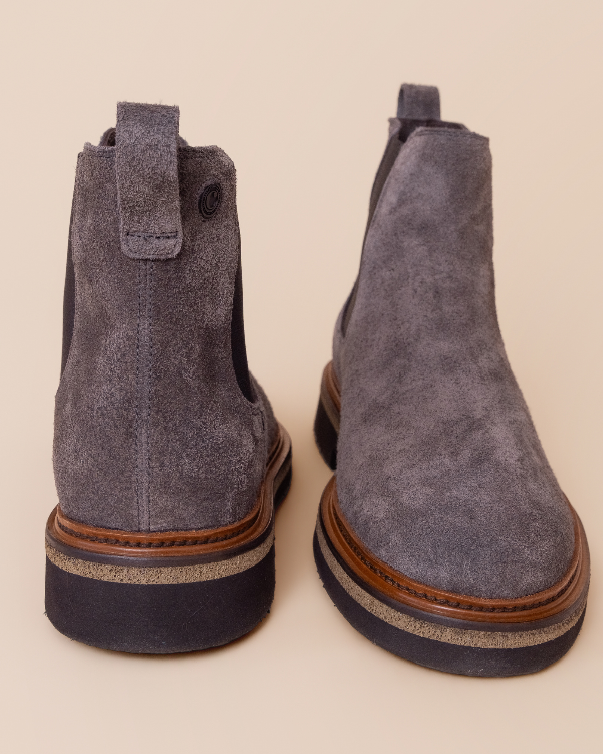 Pair of gray suede boots with brown soles on a beige background