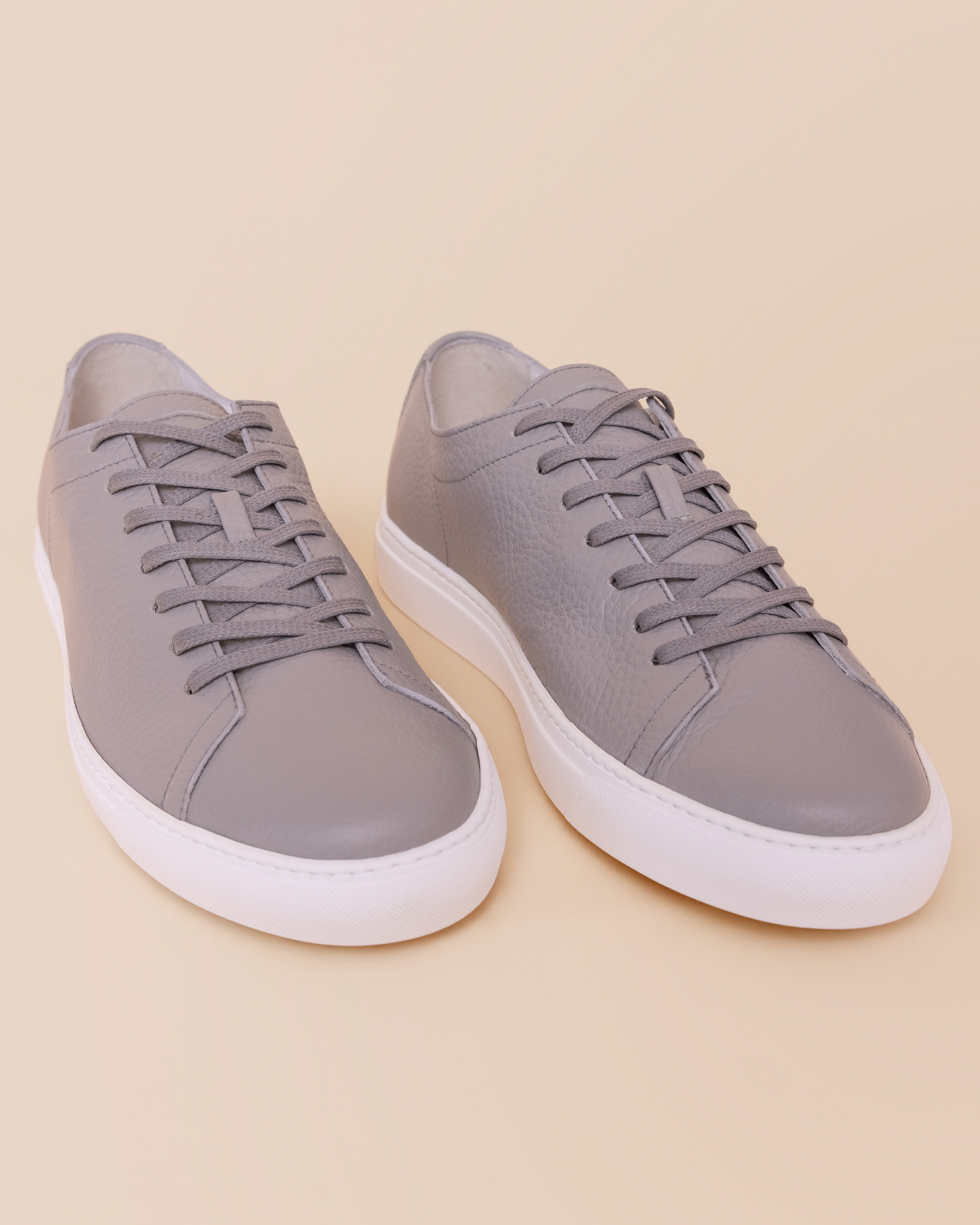 Pair of gray sneakers with white soles on a beige background