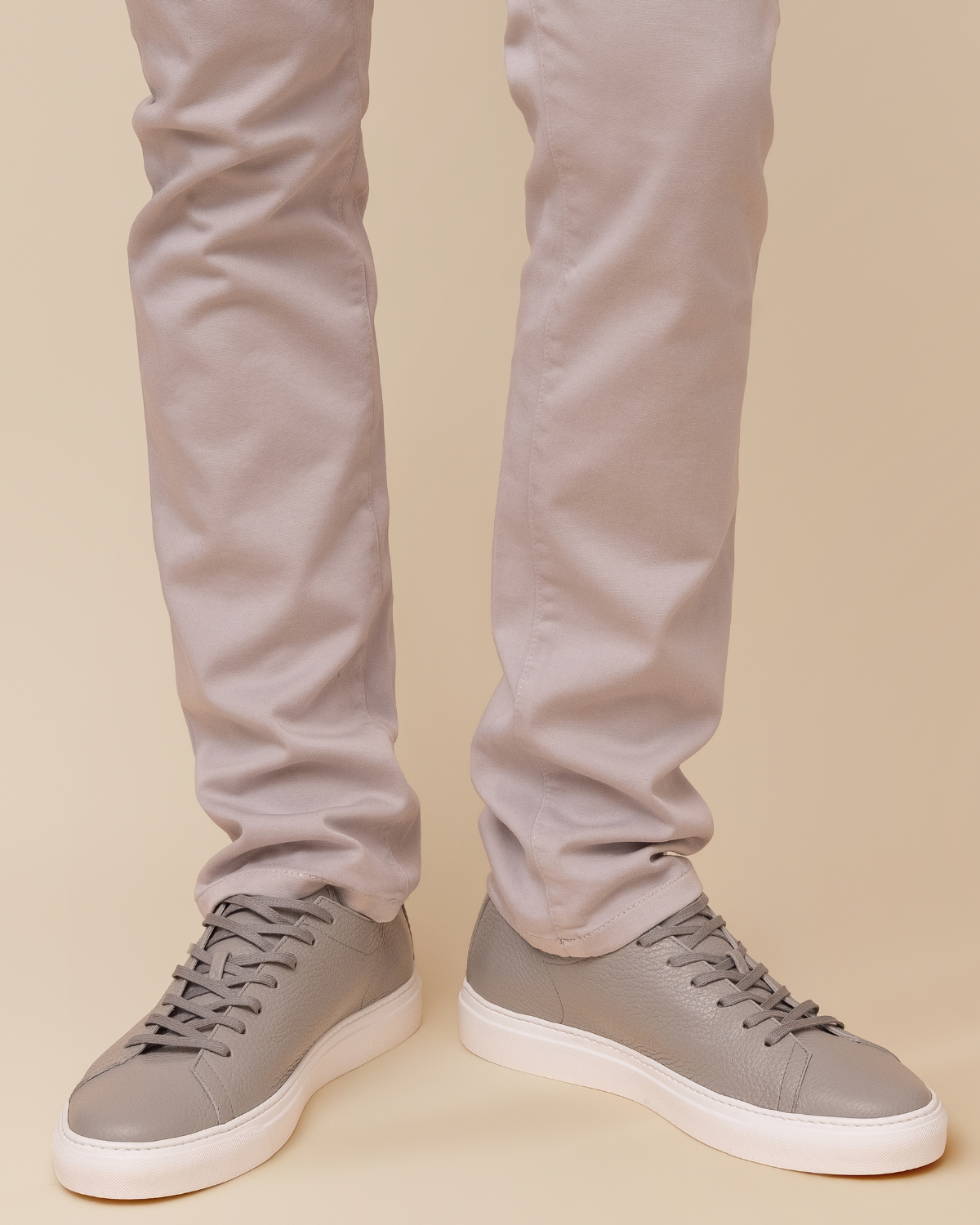Gray sneakers worn with light gray pants on a beige background