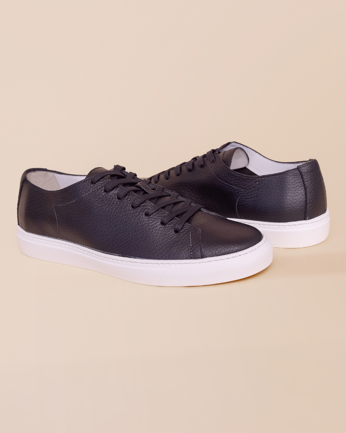 Black leather sneakers with white soles on a beige background