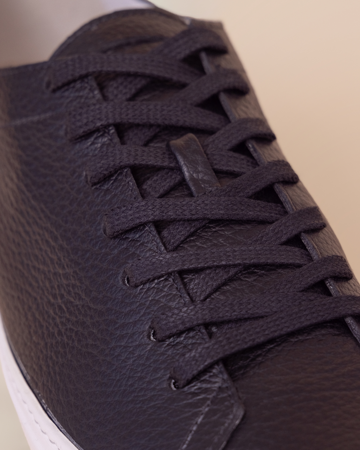 Close-up of a dark brown leather sneaker with white sole on a beige background