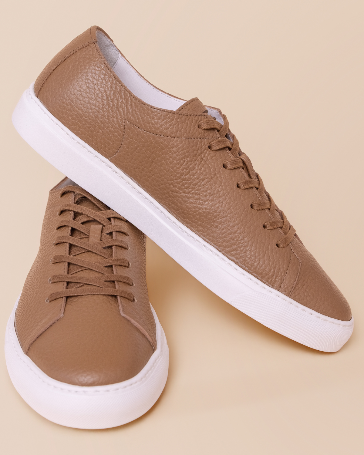 Pair of brown sneakers with white soles on a beige background