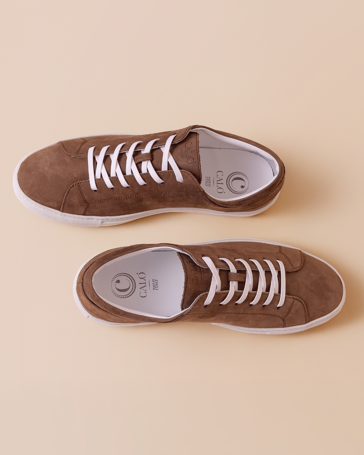Brown leather sneakers with white laces on a beige background