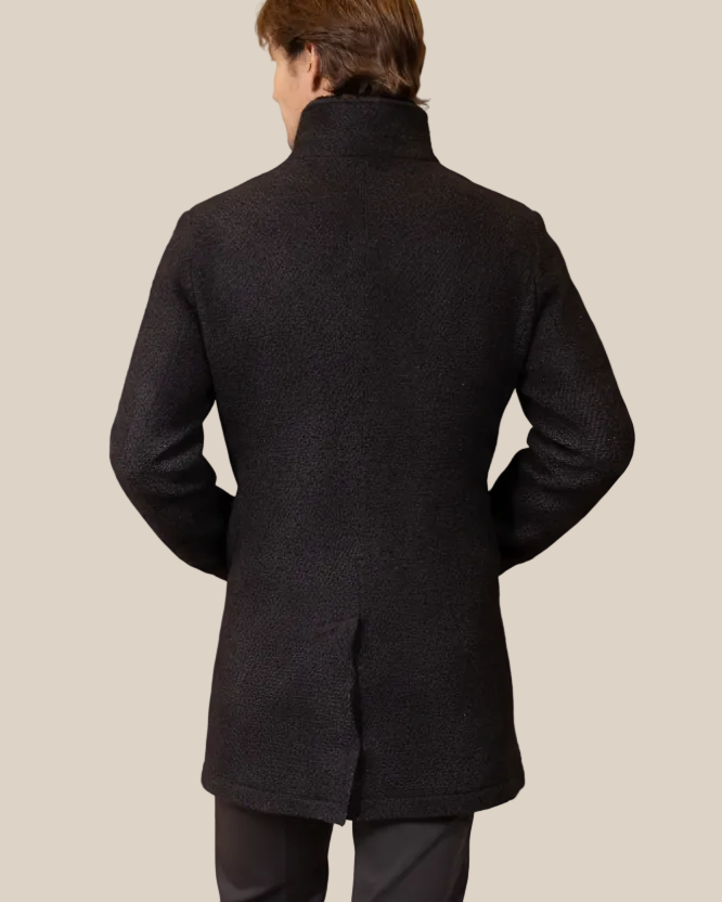 Man wearing a dark gray coat against a beige background