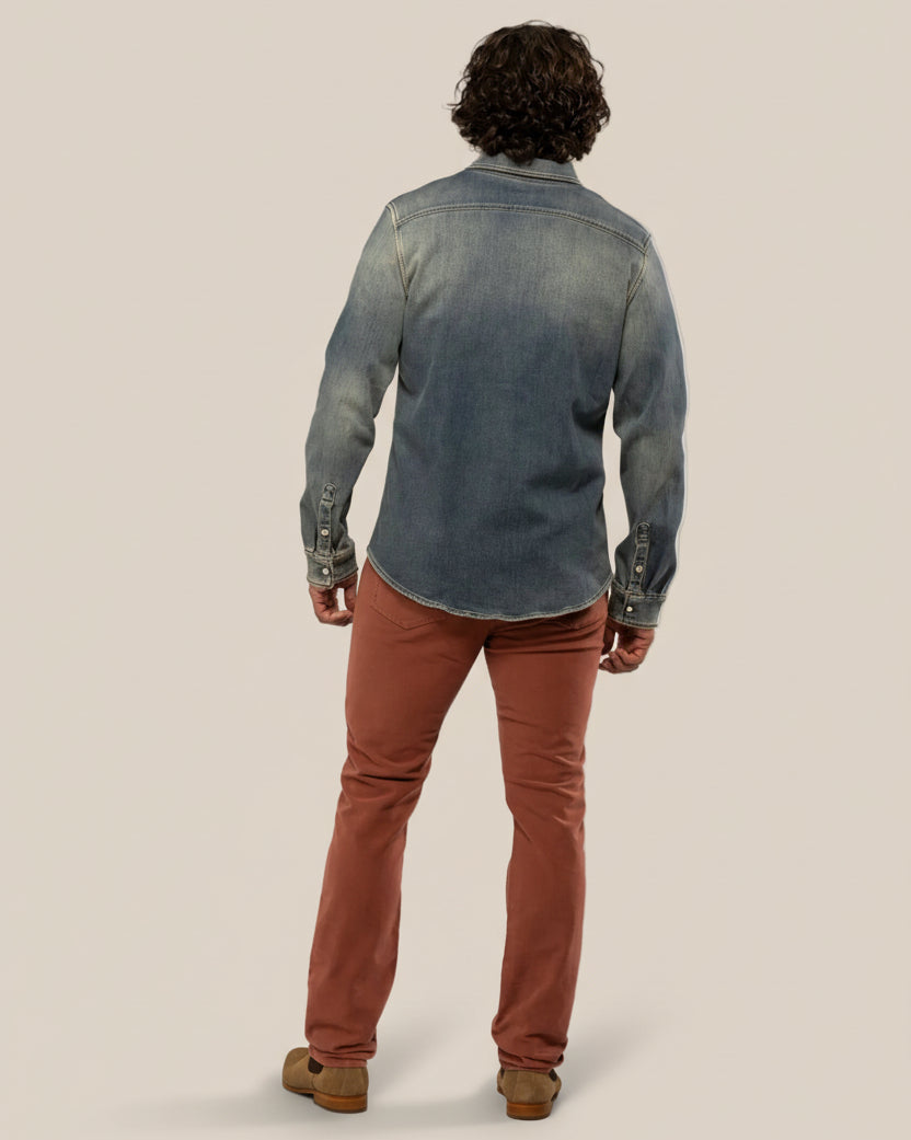 Person wearing a blue denim shirt and brown pants on a beige background