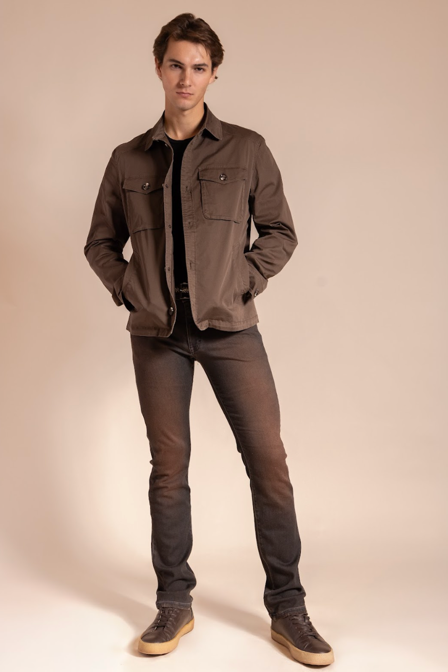 Man wearing a brown jacket and dark jeans against a beige background
