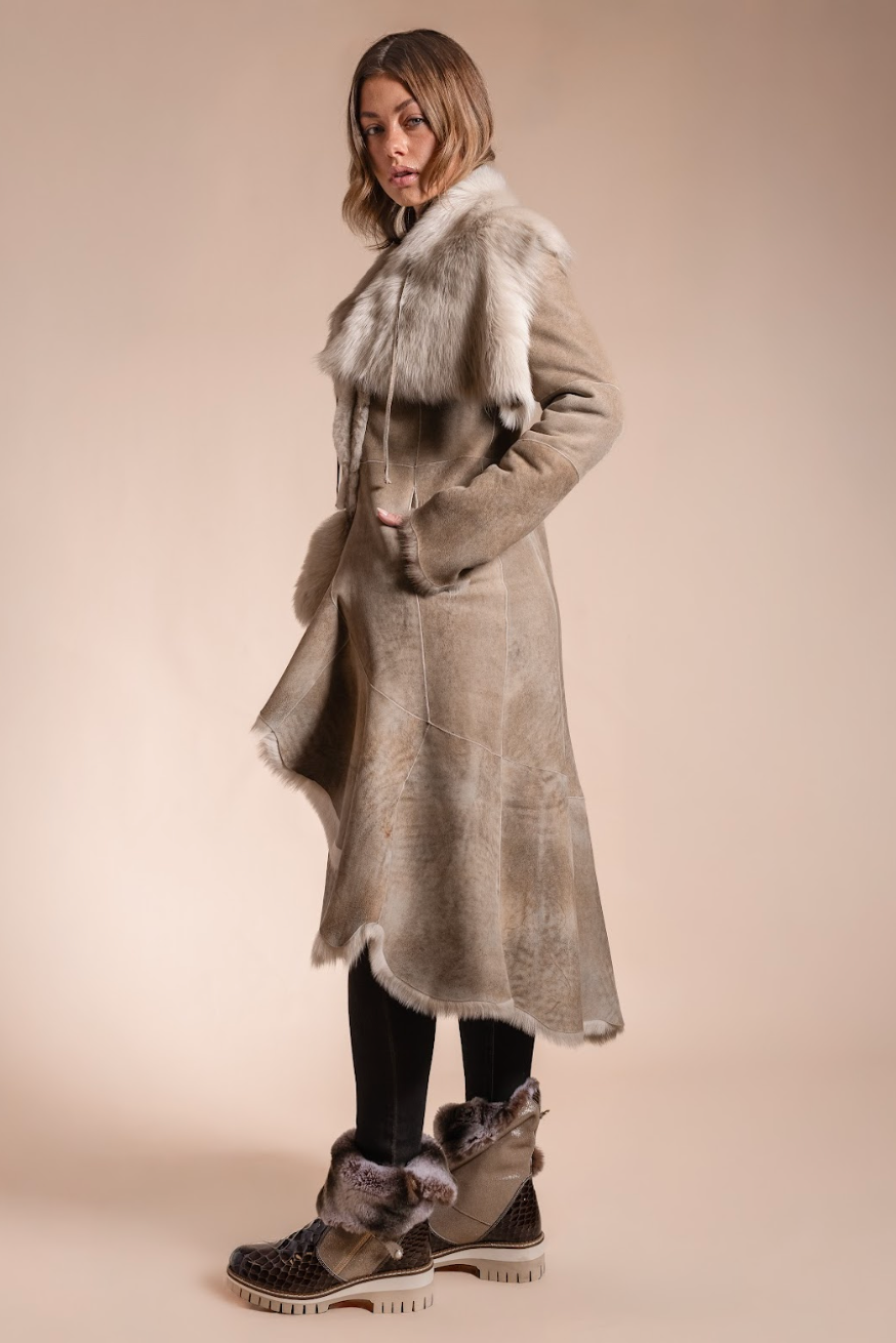 Woman wearing a long fur coat with a fur-lined hood against a beige background