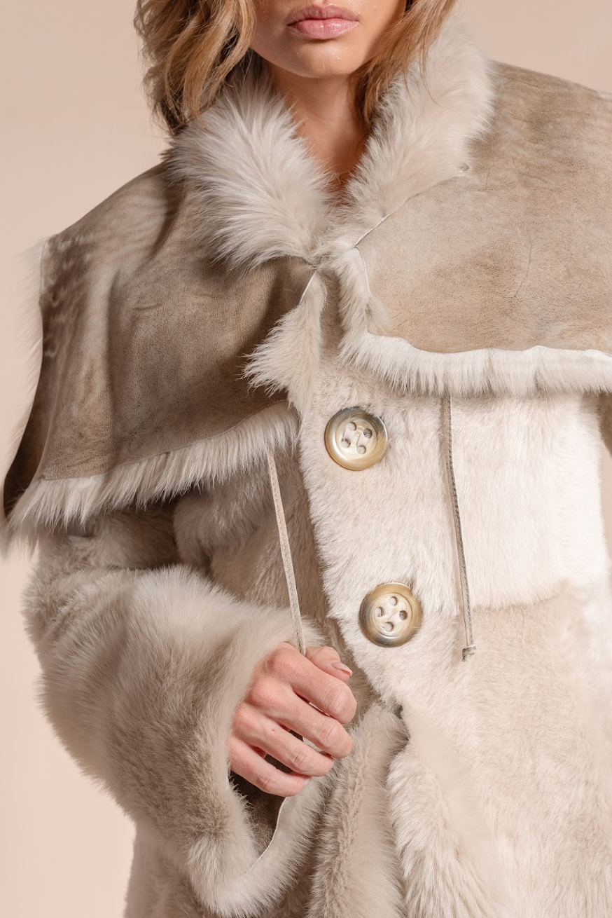 Close-up of a person wearing a fur-trimmed coat with buttons on a beige background