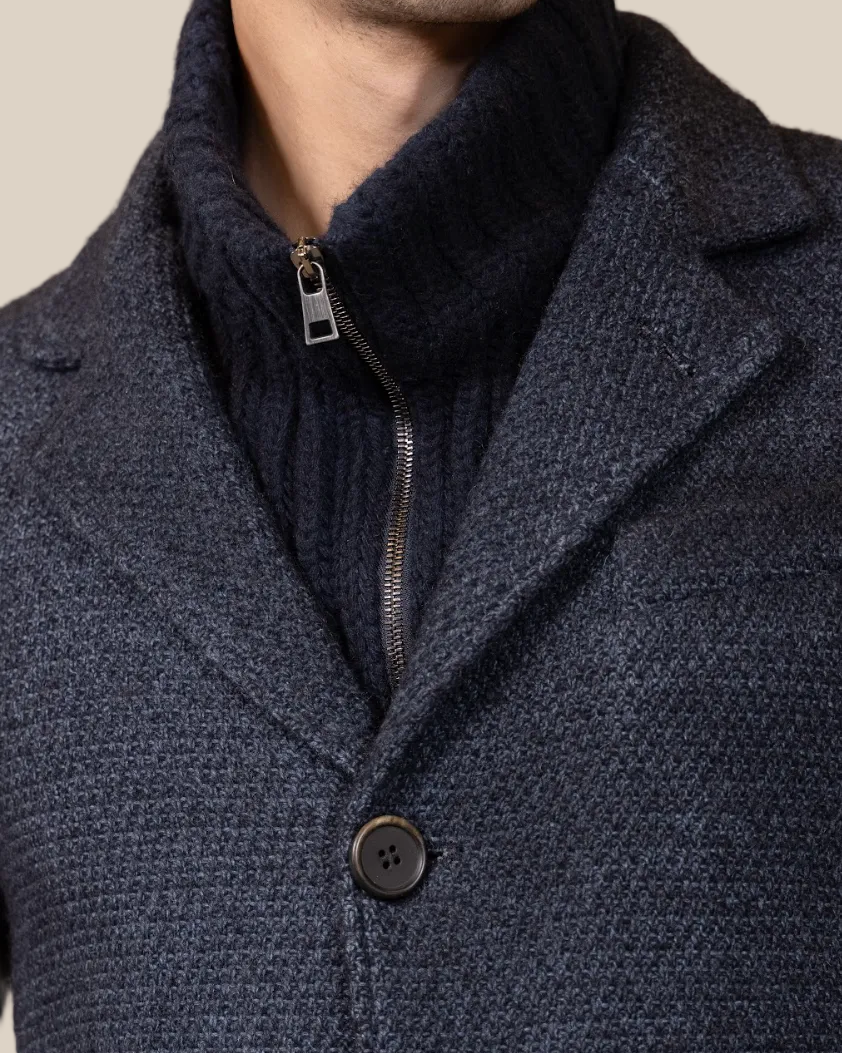 Close-up of a dark blue textured coat with a button on a brown background
