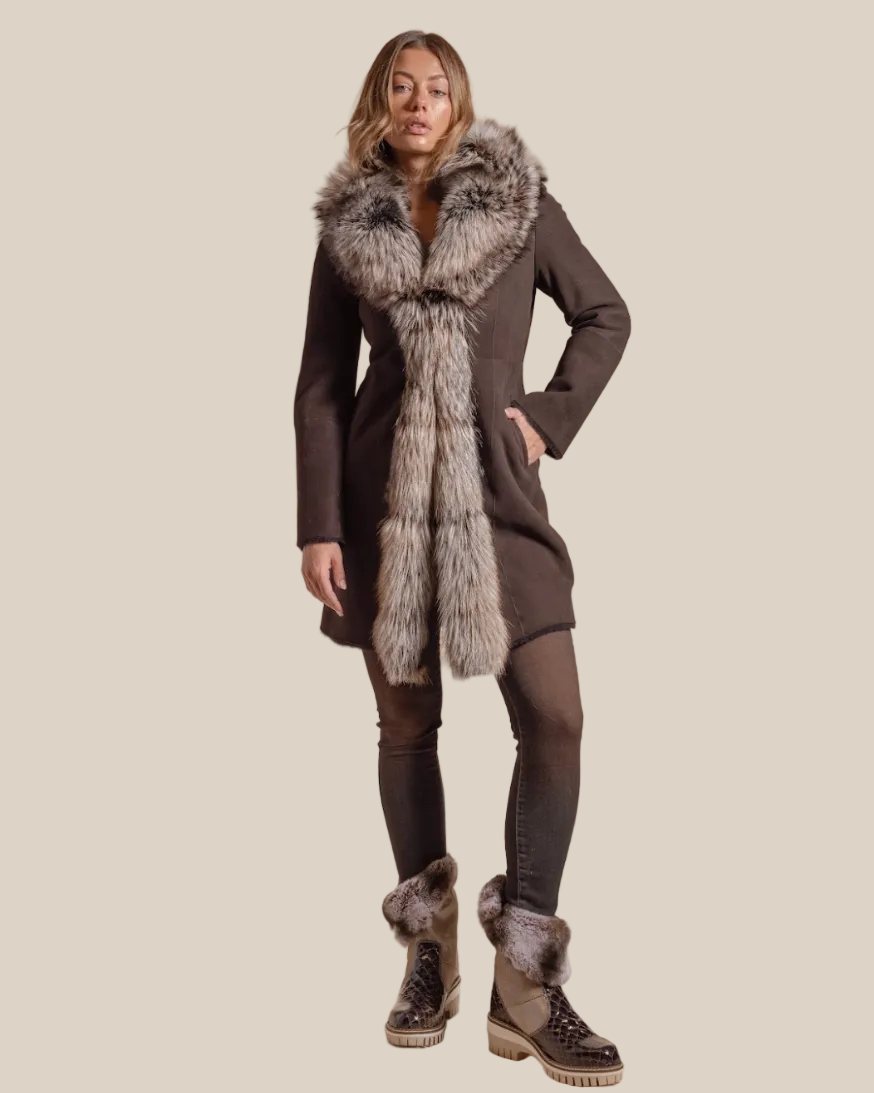 Woman wearing a long dark coat with fur trim and matching boots on a beige background