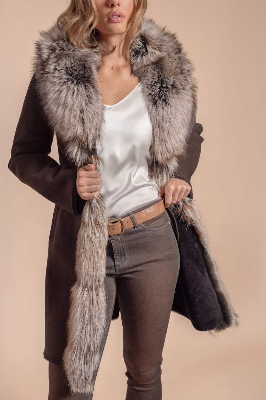 Woman wearing a long coat with a fur collar against a beige background