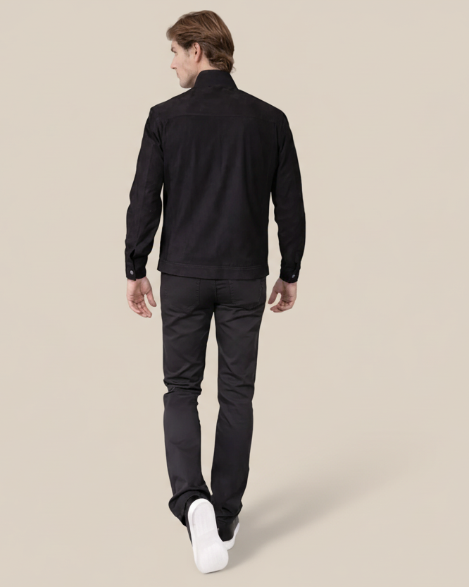 Man wearing a black jacket and pants walking on a beige background