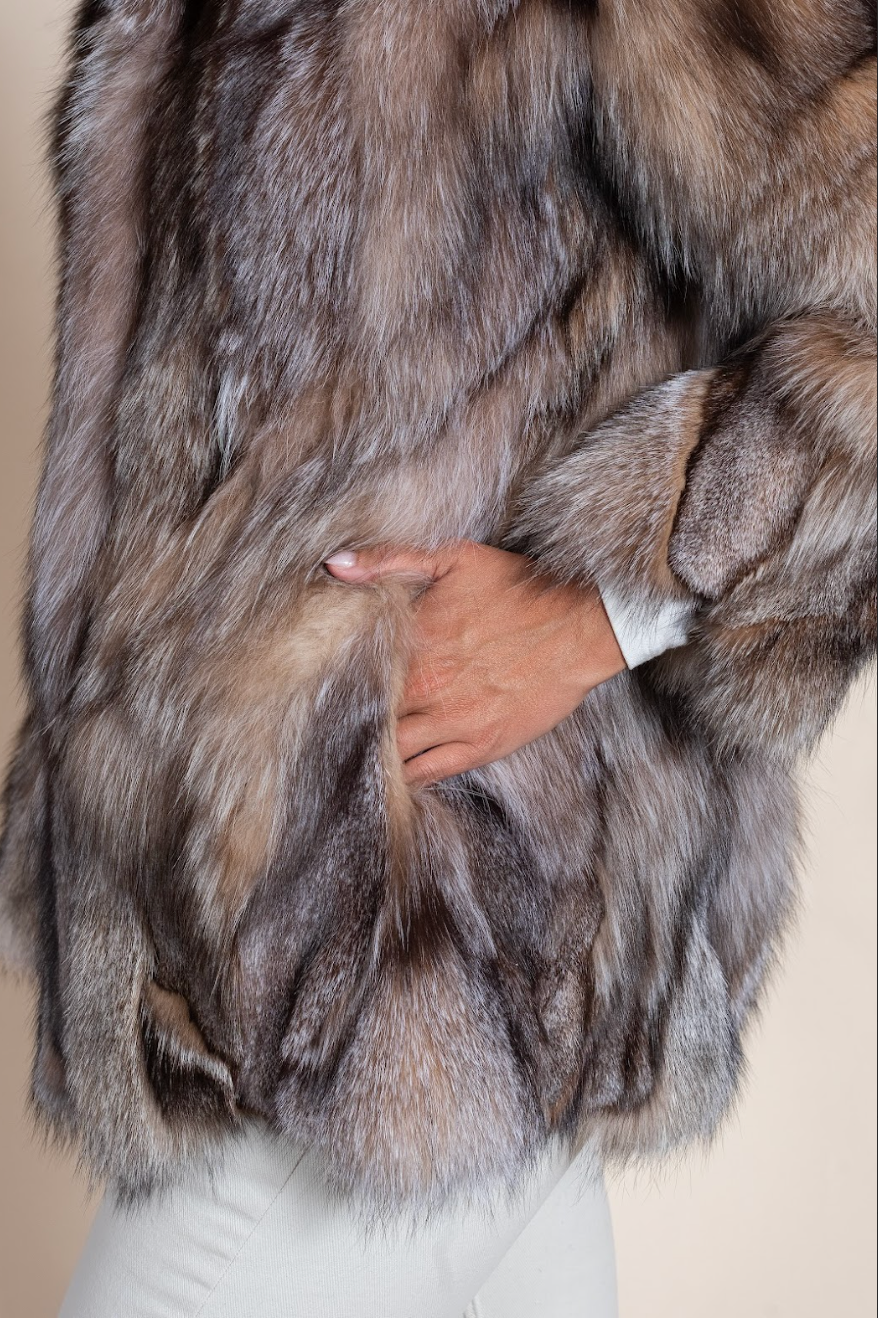 Close-up of a fur coat with a hand adjusting it against a neutral background