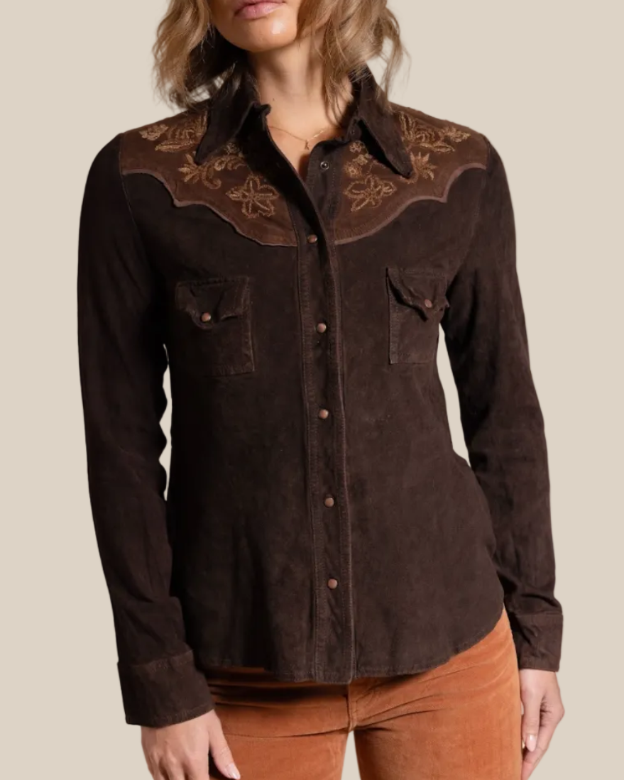 Woman wearing a brown embroidered shirt against a beige background