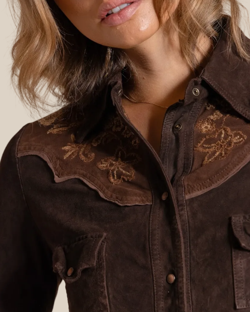 Close-up of a person wearing a brown jacket with embroidered details on a beige background