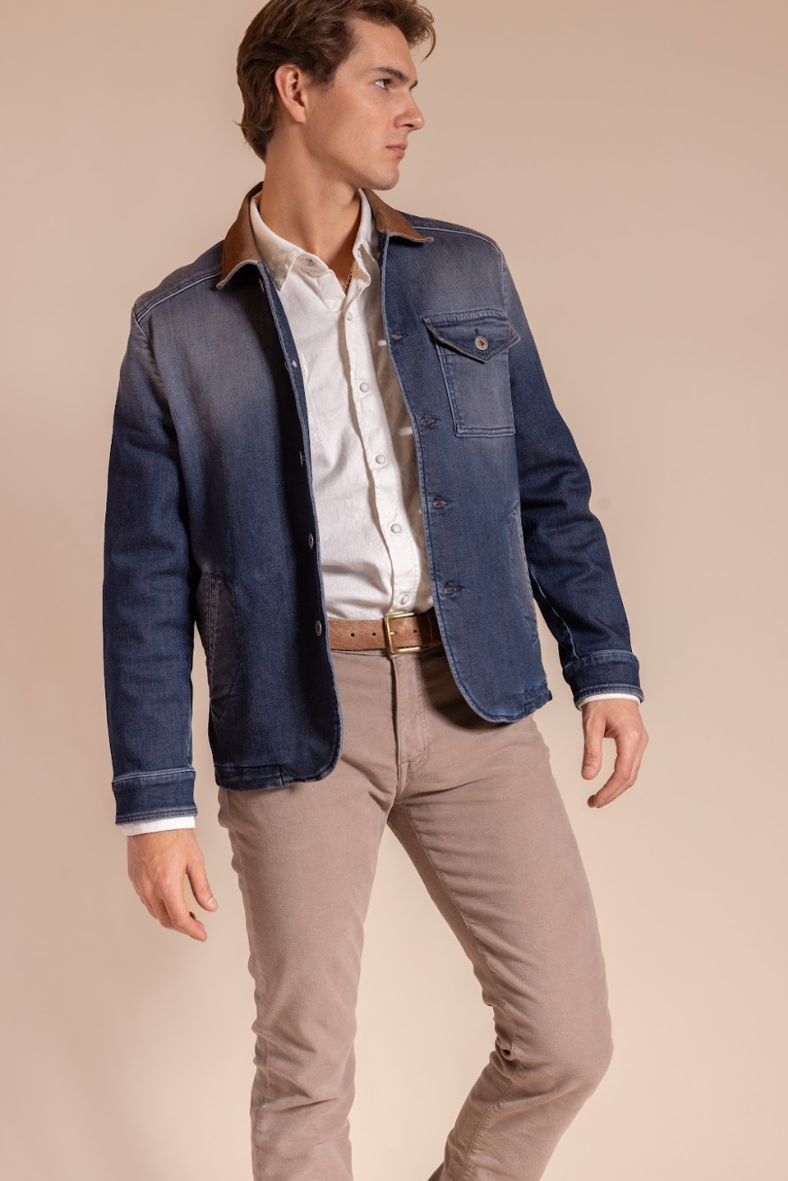 Man wearing a blue jacket over a white shirt and beige pants on a beige background