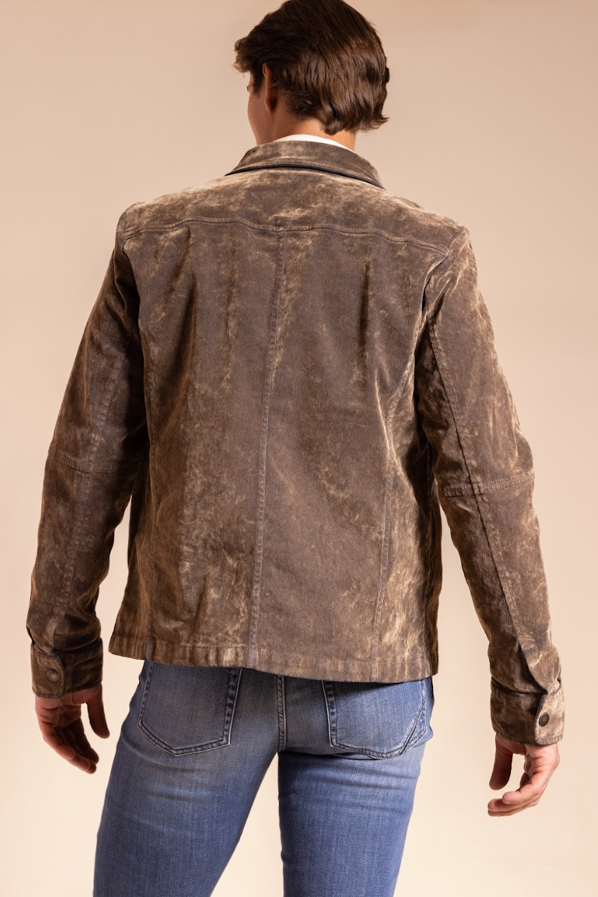 Person wearing a brown leather jacket and blue jeans on a beige background