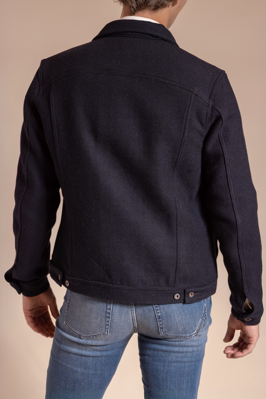 Person wearing a black jacket and blue jeans on a beige background