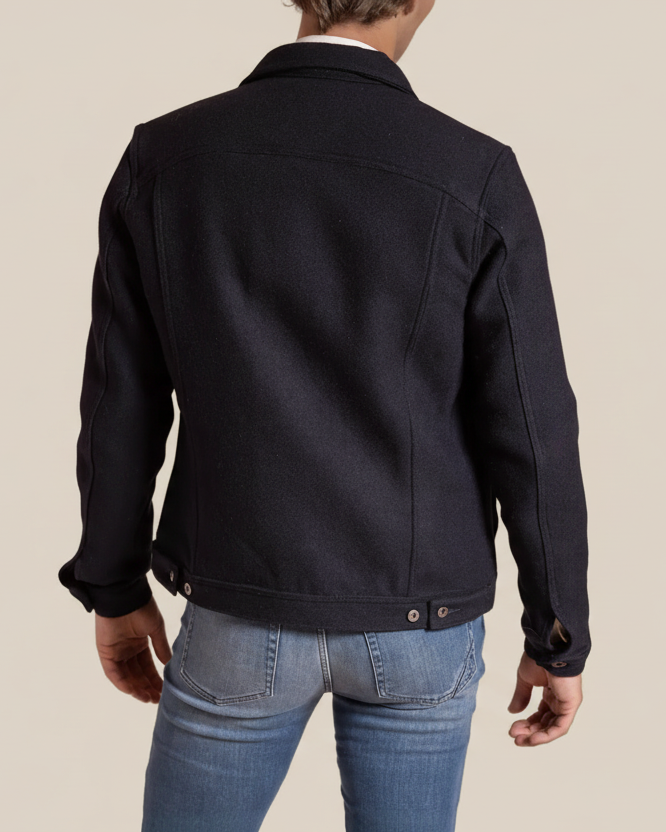 Person wearing a black jacket and blue jeans on a beige background