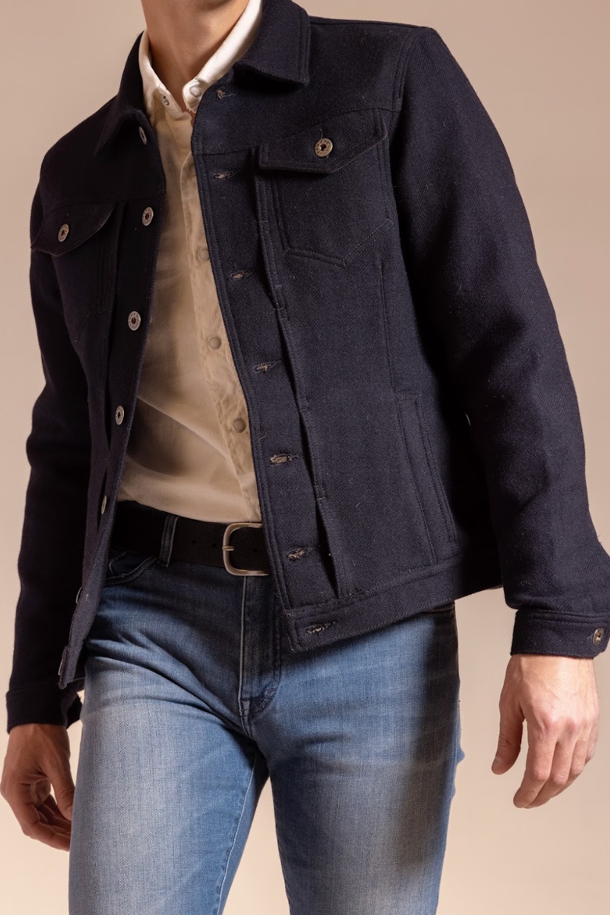 Person wearing a dark denim jacket over a light shirt and blue jeans on a beige background