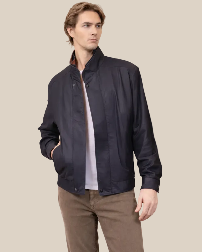 Man wearing navy lambskin bomber jacket with contrast trim, beige studio background