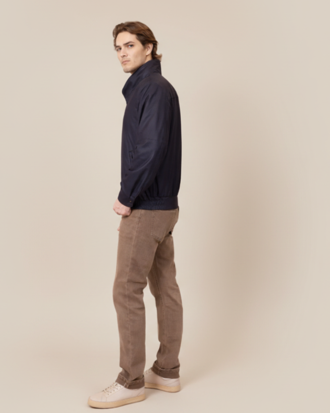 Man wearing a dark jacket and brown pants on a beige background