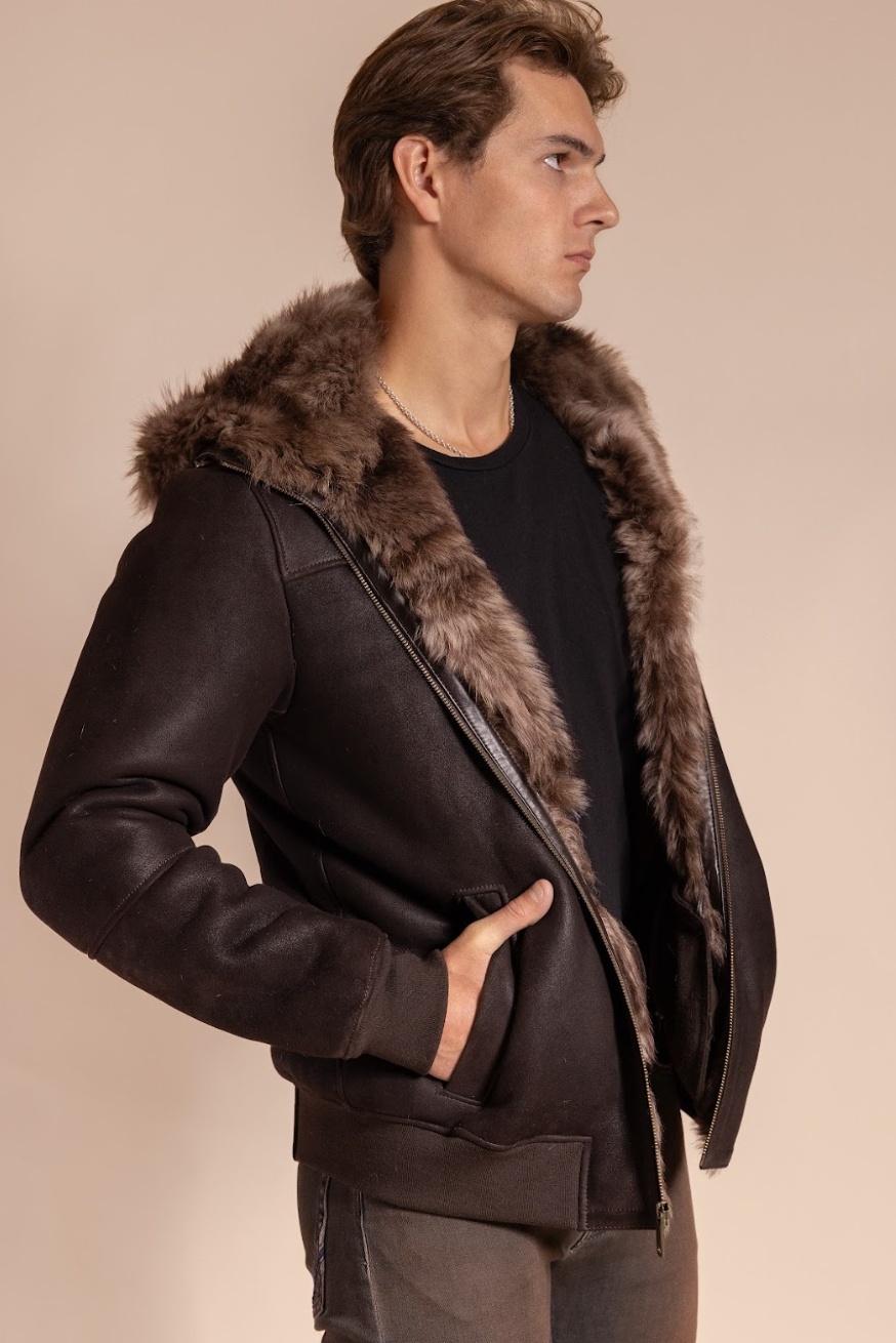 Man wearing a dark brown leather jacket with fur trim on a beige background