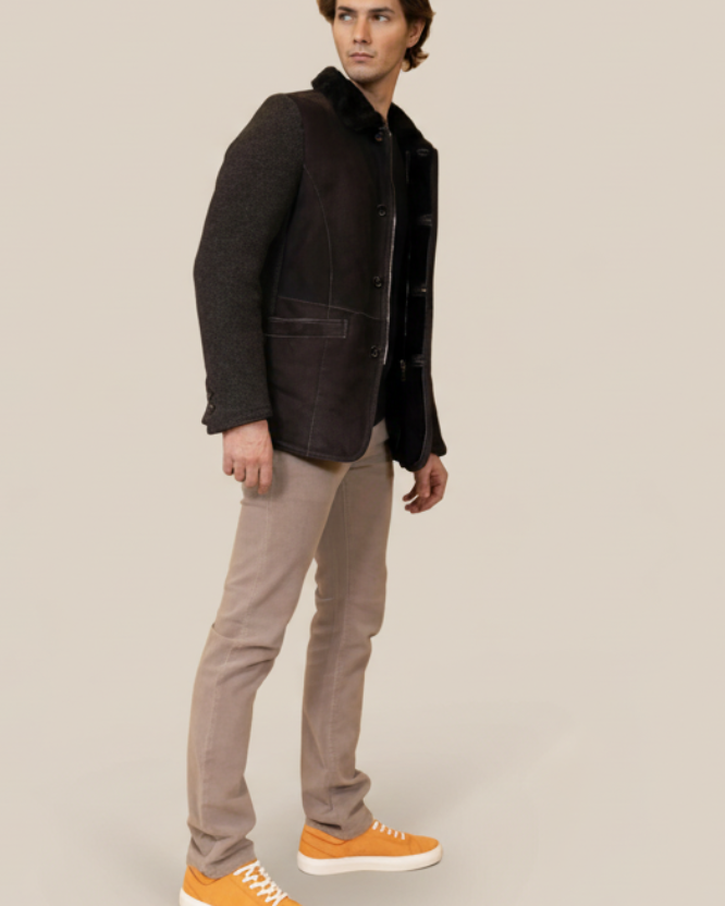 Man wearing a dark jacket, light pants, and orange shoes against a brown background