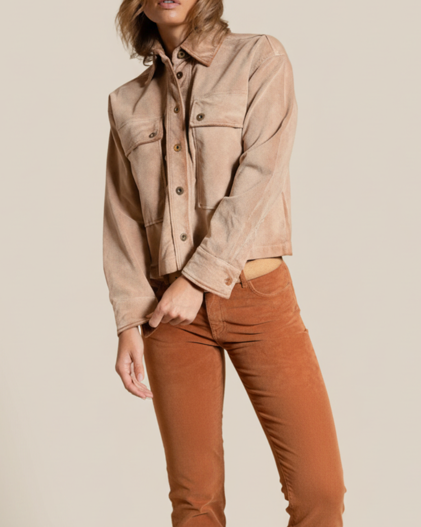 Woman wearing a beige jacket and brown pants against a neutral background