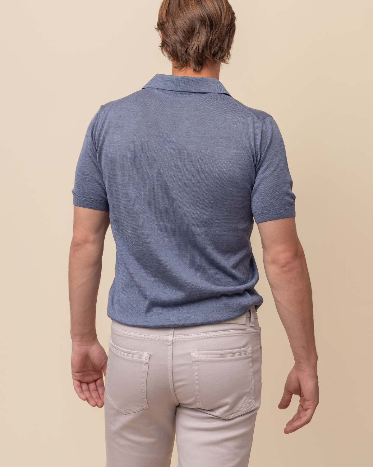 Man wearing a blue polo shirt and light-colored pants on a beige background