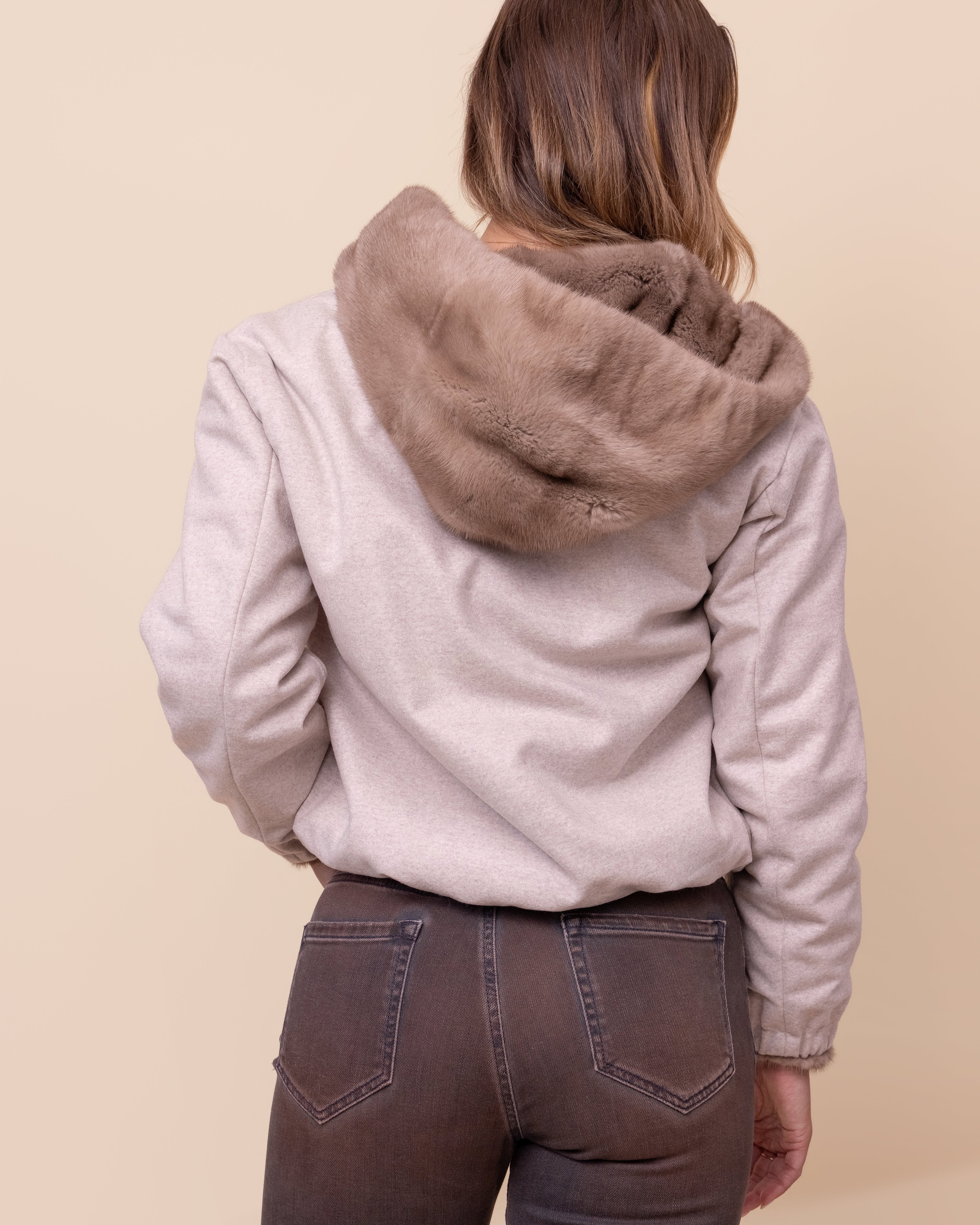Person wearing a light beige jacket with a fur-lined inside and hood on a beige backgroundand 
