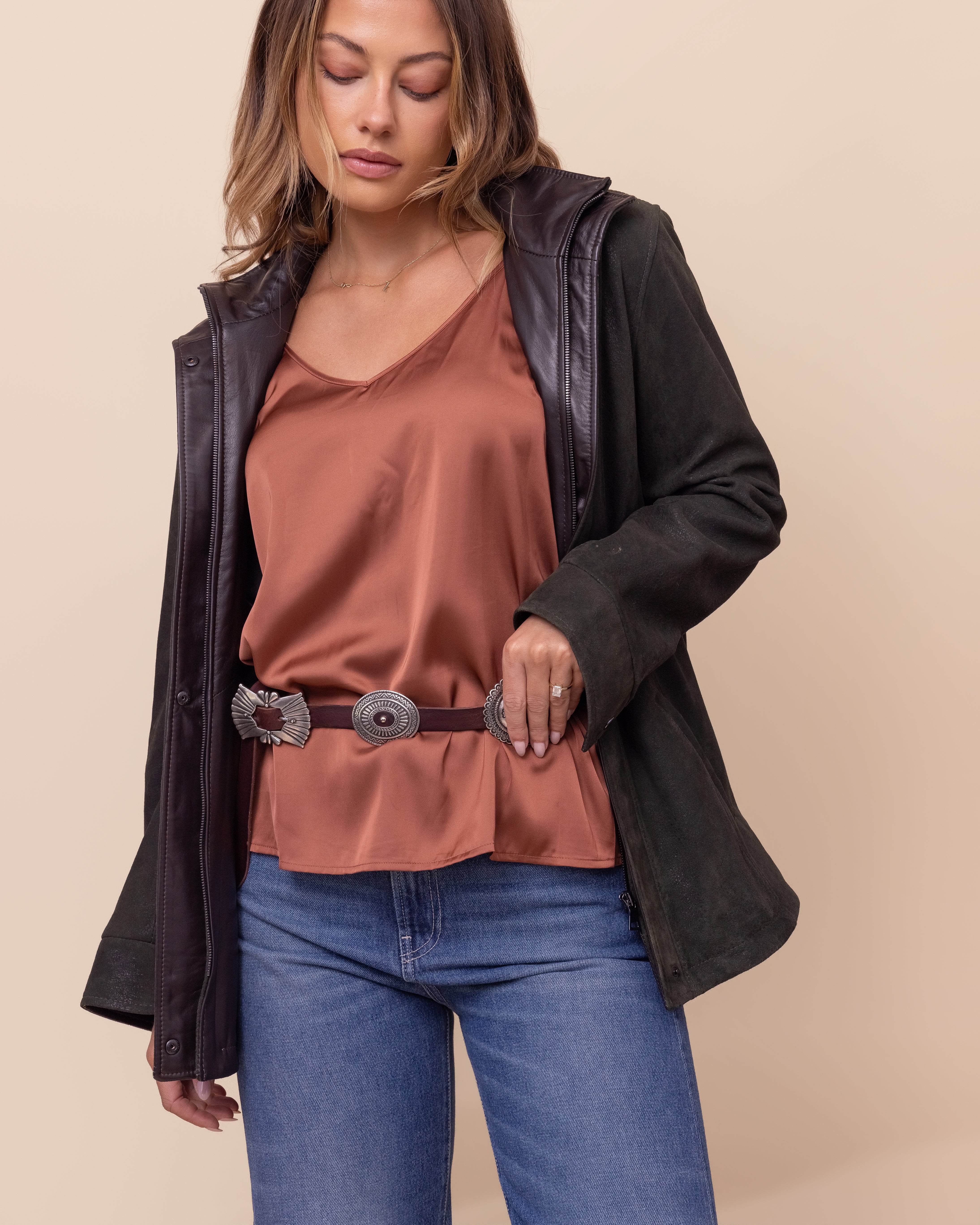 Woman wearing a brown top, blue jeans, and a green jacket on a beige background