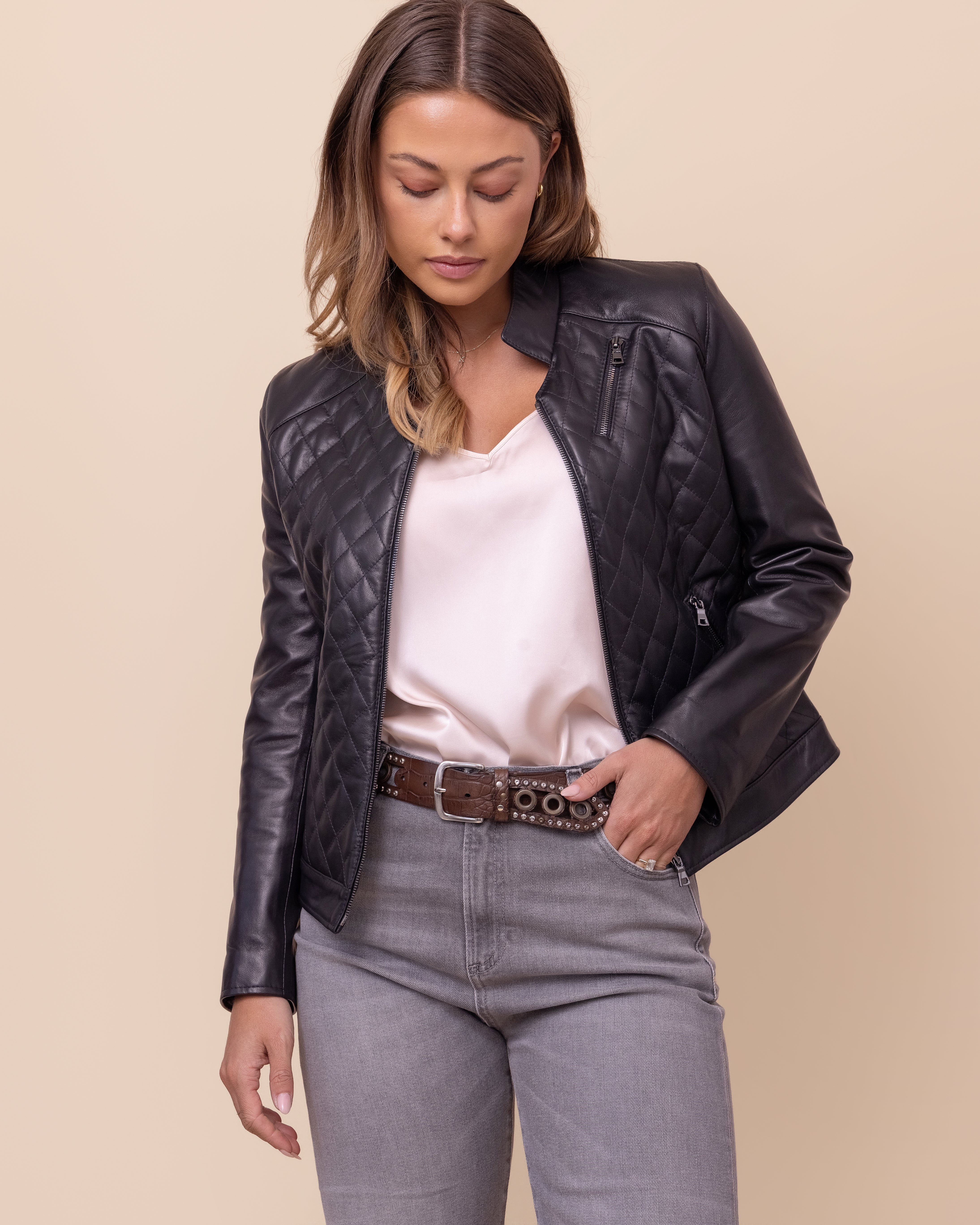 Woman wearing a black leather jacket, white shirt, and gray jeans on a beige background