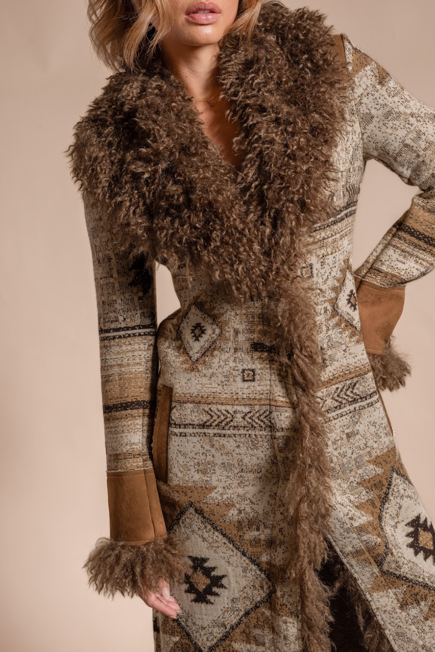 Person wearing a patterned coat with fur collar and cuffs on a beige background